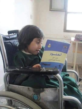 صورة طفل من ذوي الإعاقة الحركية يمسك كتاب مدرسي